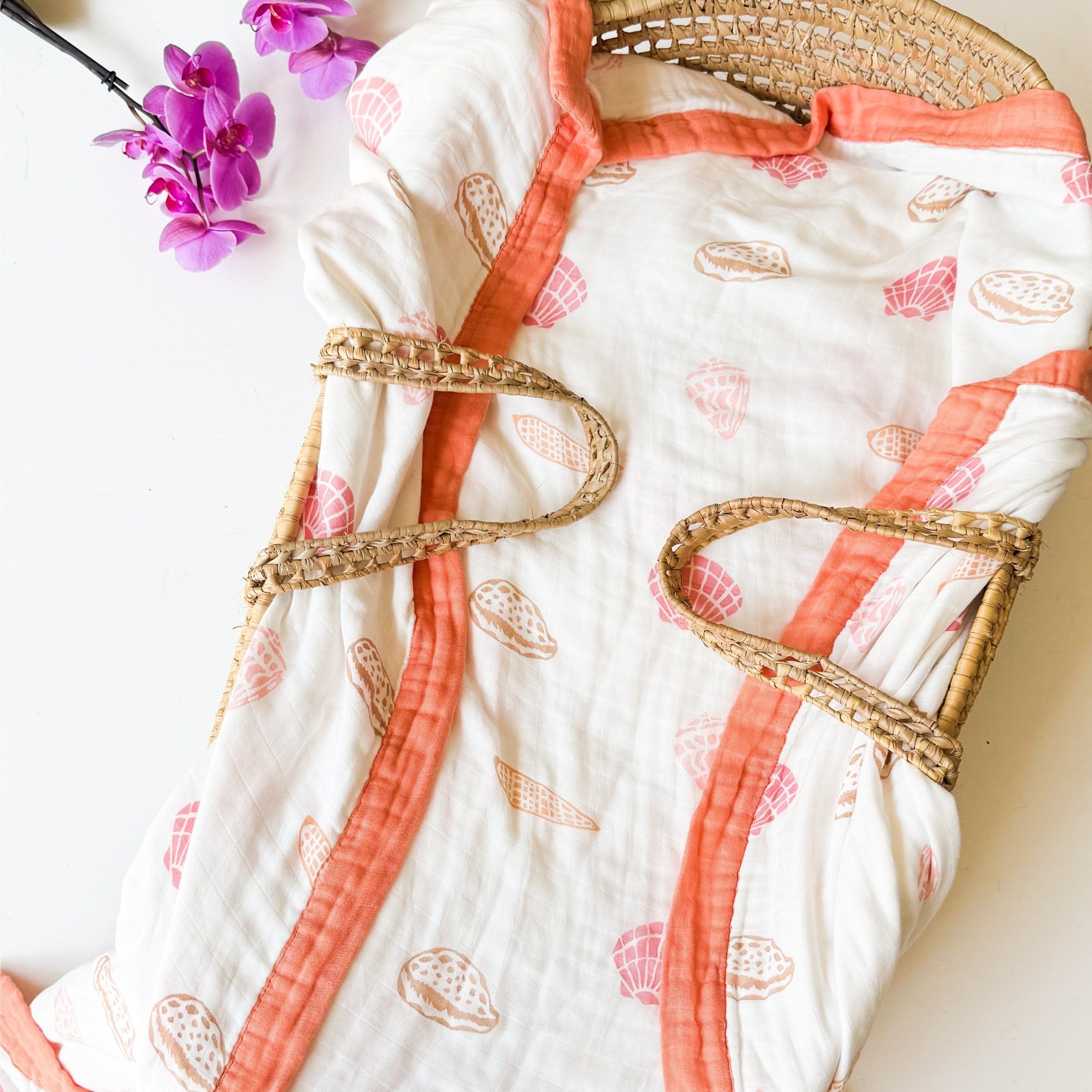 organic seashell print luxe baby blanket. Beige, soft pinks, oranges with coral trim.