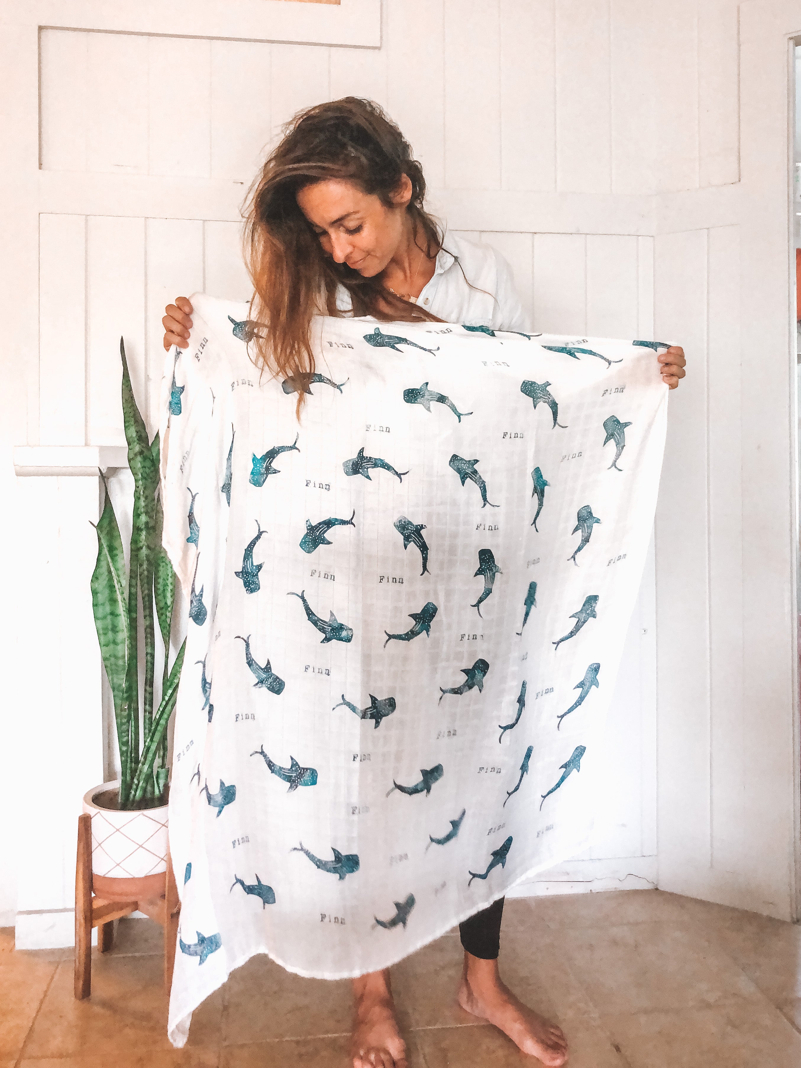 Coca + B. Owner and Designer Molly Sanders holding handmade organic muslin baby swaddle with whale sharks.